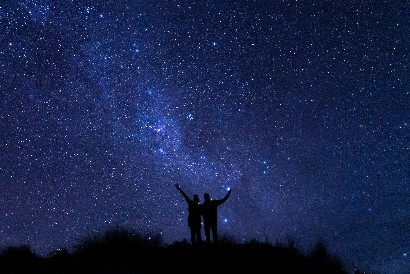 silhouette of man standing on grass field under starry night