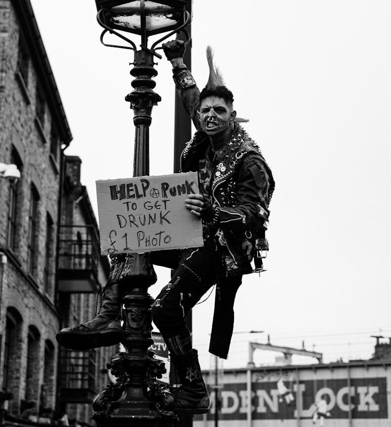 grayscale photo of man in jacket and pants holding signage